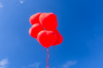 Fototapeta na wymiar Red heart shaped helium balloons flying in the sky