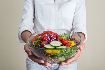 hands of beautiful woman holding big bowl of fresh veggie salad