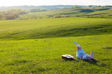 Beautiful hippie girl with guitar lying on grass