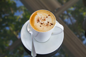 A cup of coffee in a white cup on glass background