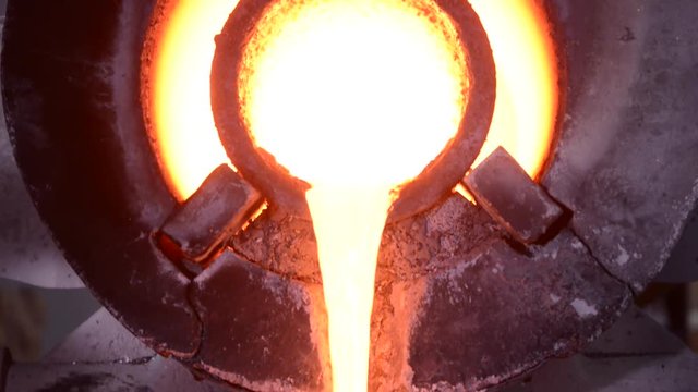 Steel worker in protective clothing raking furnace in an industrial foundry