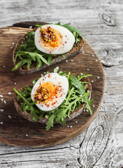 Sandwich with arugula, boiled egg and mustard on a wooden board. Healthy breakfast or snack