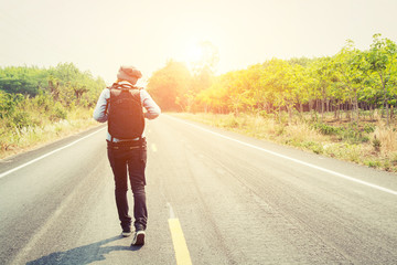 Fototapeta premium Rear view of a young woman hitchhiking carrying backpack walking