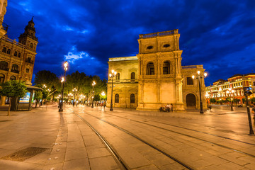 Fototapeta na wymiar Tram tracks, historic buildings and the streets of the center of Seville illuminated by night. Seville town, Andalusia, Spain.