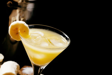 Yellow cocktail with whiskey, banana and ice, black background,