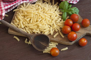 Dried pasta, tomatoes, basil on wooden background