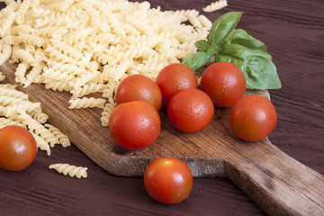 Dried pasta, tomatoes, basil on wooden background