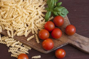 Dried pasta, tomatoes, basil on wooden background