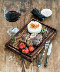 Roast beef Ossobuco with rice, vegetables and glass of wine on serving board over rustic wood background