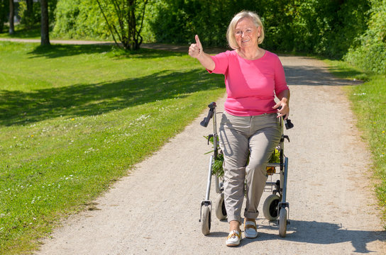 Elderly woman sits in wheeled walker on park path