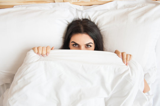 Smiling girl in bed covering her face under blanket