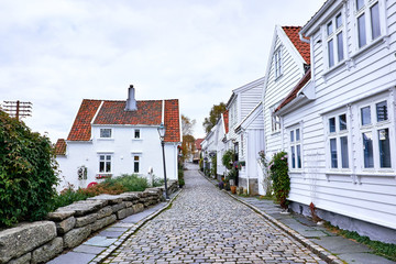 Fototapeta na wymiar Old white painted town houses made of wood, next to a cobblestone street in Old Stavanger in Norway