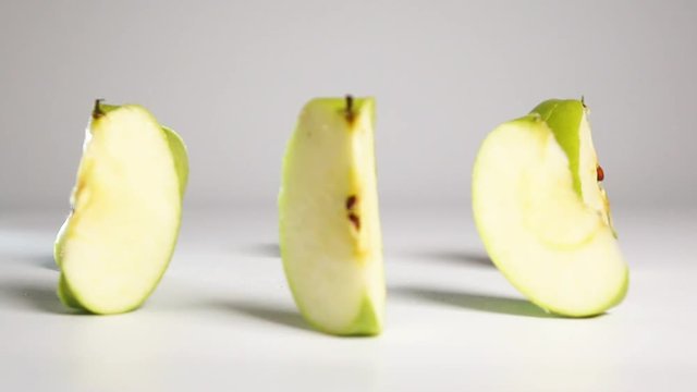 Fresh tasty green apple breaking up into pieces and rolling onto it sides on dry white floor. Shoot with high speed camera in slow motion mode. White background isolated.