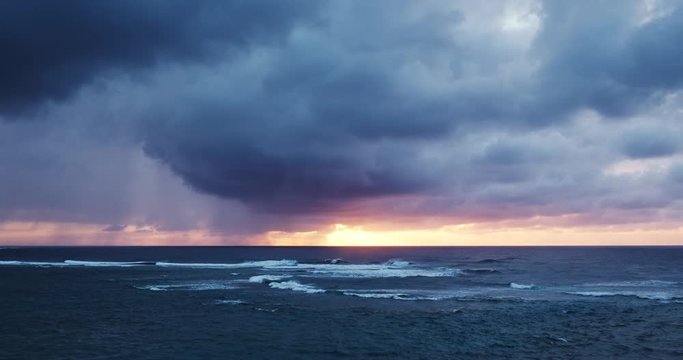 Aerial view flying over ocean reef and waves into dramatic sunset storm on the north shore of Kauai