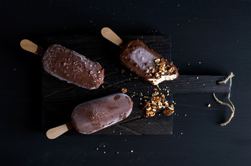 Chocolate dipped popsicles with chipped nuts on dark wooden board over black background