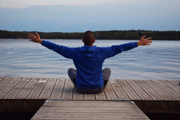 Young happy man meditating on a pier - beautiful landscape background (wallpaper)