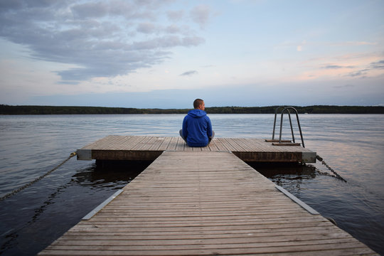 Young happy man meditating on a pier - beautiful landscape background (wallpaper)