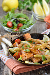 Gebratener bayerischer Spargel mit Lachsstreifen in der Eisenpfanne mit Rucola-Beilagensalat serviert - Roasted  white asparagus with fried salmon served in an iron frying pan with a rocket side salad