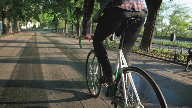 Young hipster man riding gixed gear bike on the road  in park, slow motion