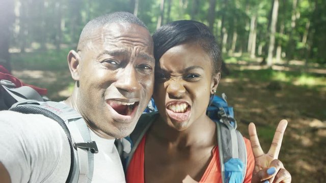  Portrait of attractive couple hiking in the woods, pulling faces to camera