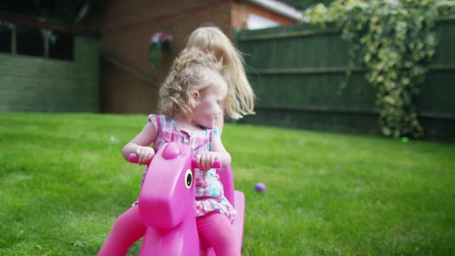  Toddler girl playing in the garden with older sister, on rocking toy