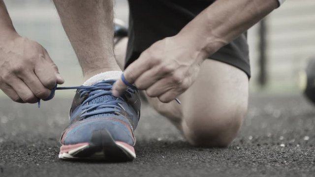 unrecognisable man in urban area ties his shoelaces during workout