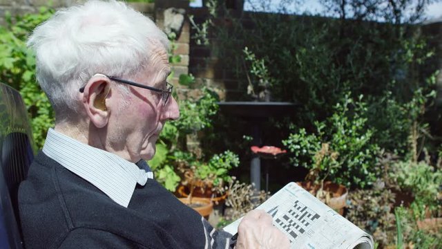  Elderly Man In The Garden Doing A Crossword Puzzle In The Newspaper