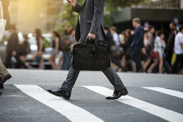 Businessman crossing the street on crosswalk and honding a laptop bag and smatphone in the city © Nick Starichenko
