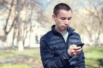 The young successful man with a mobile phone on the background of the spring streetscape .