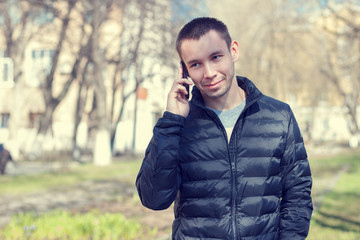 The young successful man with a mobile phone on the background of the spring streetscape .