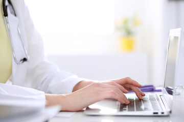 Fototapeta premium Close-up of female doctor typing laptop sitting at a table in the hospital