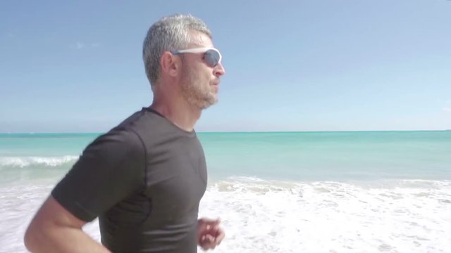 male runner wearing sport glasses working out running on beach steadicam