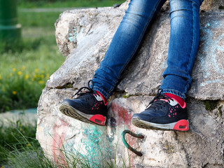 Obraz premium Legs of a teenager. Jeans, sneakers. Old dirty concrete wall. The concept - nature of adolescent behavior. Green grass