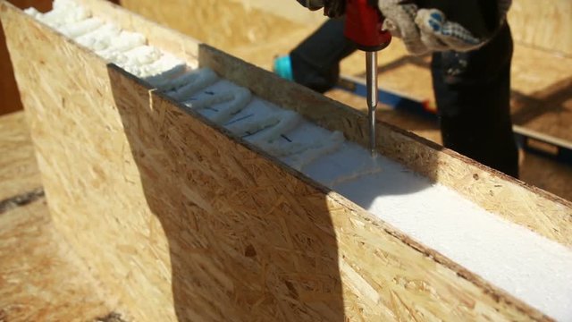 Worker applying polyurethane expanding foam glue with gun applicator. building houses of foam panels and plywood