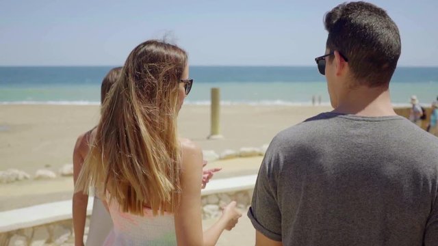 Group of trendy young tourists out sightseeing walking along a beachfront promenade at a resort