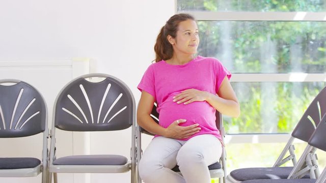  Happy pregnant woman rubs her belly as she waits to see the doctor 