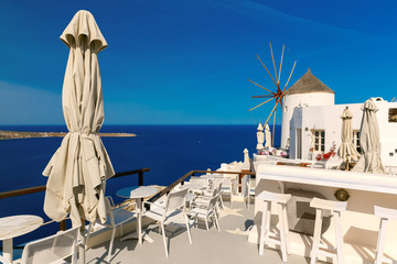 Picturesque view of windmill, empty restaurant and white houses in Oia or Ia on the island Santorini, Greece