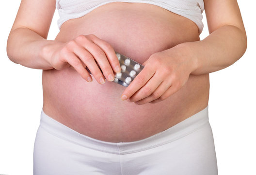 Pregnant woman holding pills closeup on white