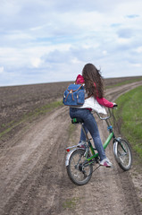 Fototapeta na wymiar The girl goes on a bicycle on the road in a field