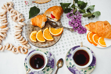 Beautiful and healthy Breakfast: croissants and coffee on the table with oranges and lilac flowers