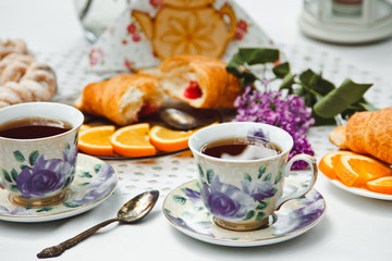 Beautiful and healthy Breakfast: croissants and coffee on the table with oranges and lilac flowers