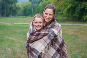 Fototapeta premium Young sister and brother stand covered with plaid in park.