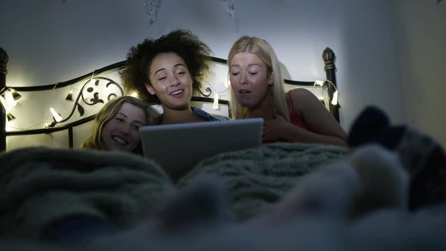  Young female friends having a sleepover, watching film or tv on computer
