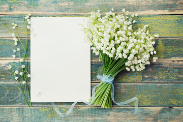 Bouquet of flowers lily of the valley and empty paper sheet on rustic table from above, beautiful...