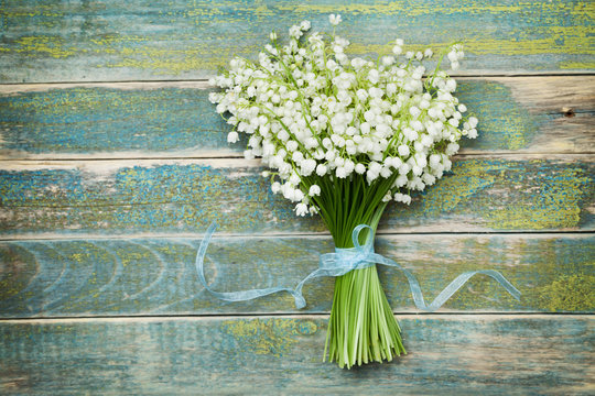 Beautiful bouquet of flowers lily of the valley on vintage wooden table from above, rustic background