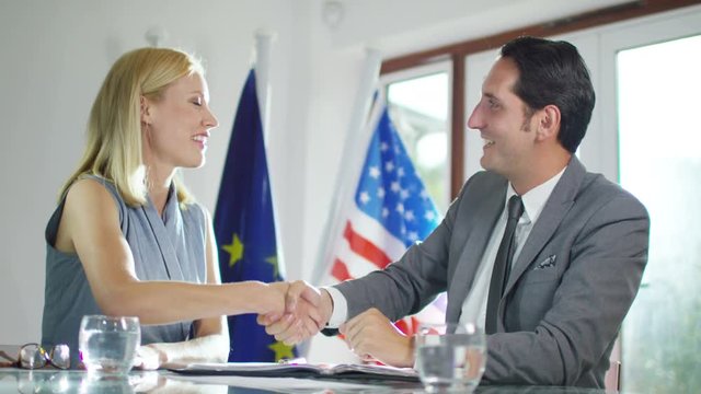  Male & female diplomats in office sign an agreement & shake hands on the deal