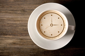 Cup of coffee with clock drawing on foam, top view