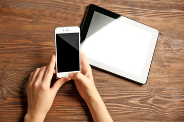 A tablet and female hands using mobile phone, on the wooden background