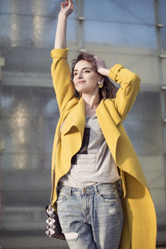 Young Woman In A Yellow Coat On A Background Of City