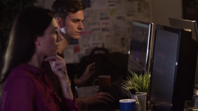  Young man & woman working side by side on computers in creative office